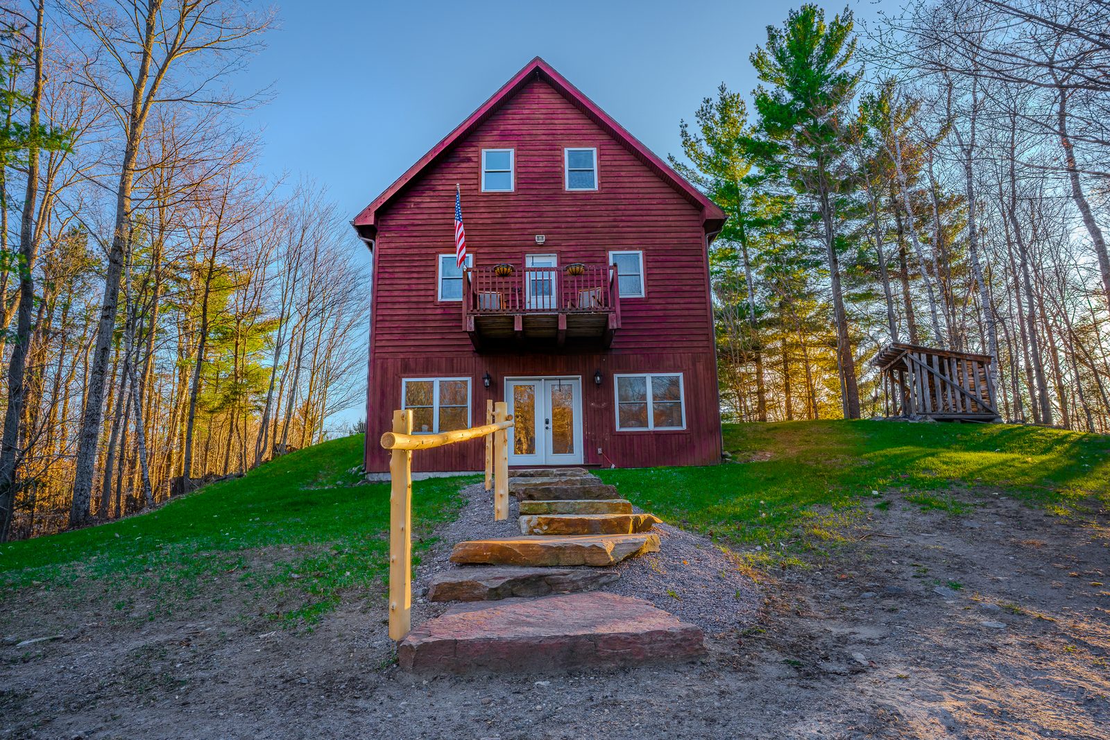 Red farmhouse twilight, American flag, lit windows